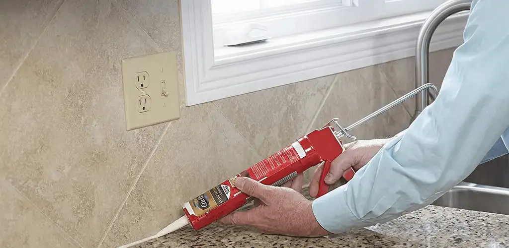 Handyman applying caulk along a kitchen backsplash and countertop seam in Sterling Heights, MI