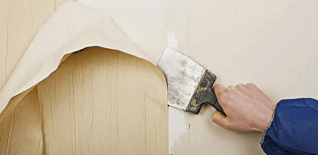 Handyman removing wallpaper with a scraper for wall preparation in Sterling Heights, MI