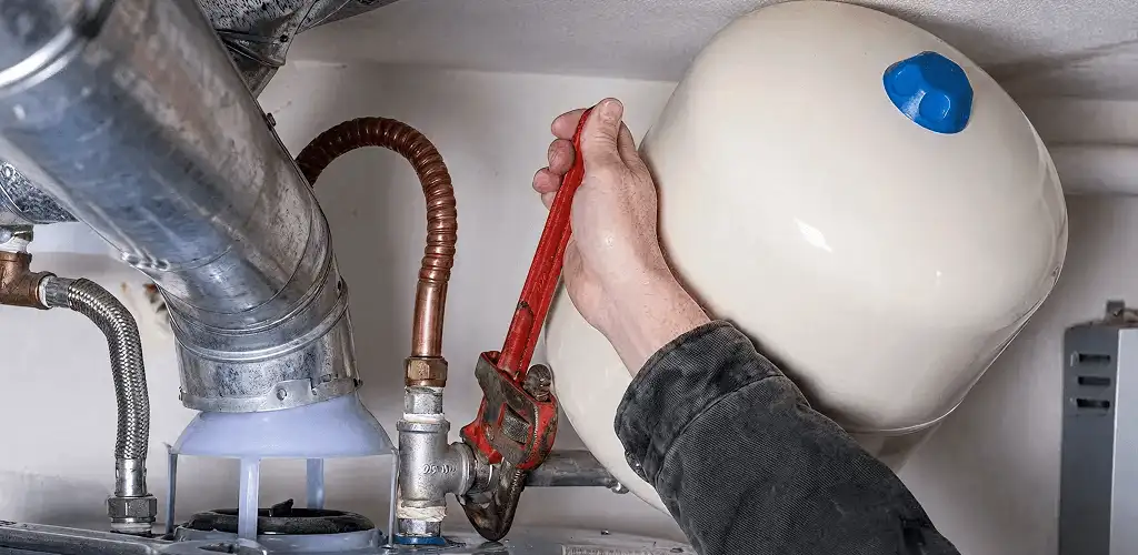 Water heater repair technician tightening plumbing connections near a tank unit in Sterling Heights, MI